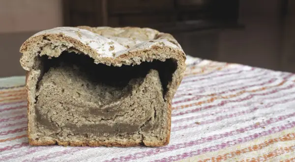 Przekrojony bochenek chleba drożdżowego z pustym środkiem, leżący na kolorowym obrusie.