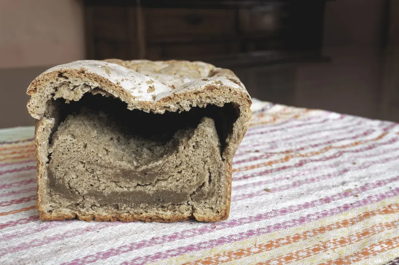Przekrojony bochenek chleba drożdżowego z pustym środkiem, leżący na kolorowym obrusie.