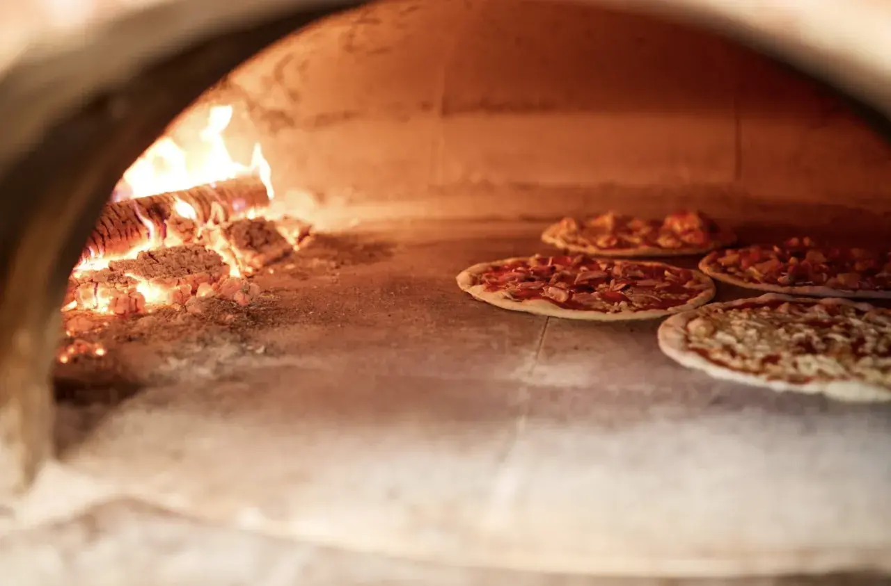 duży piec do pizzy opalany drewnem z czterema pizzami w środku