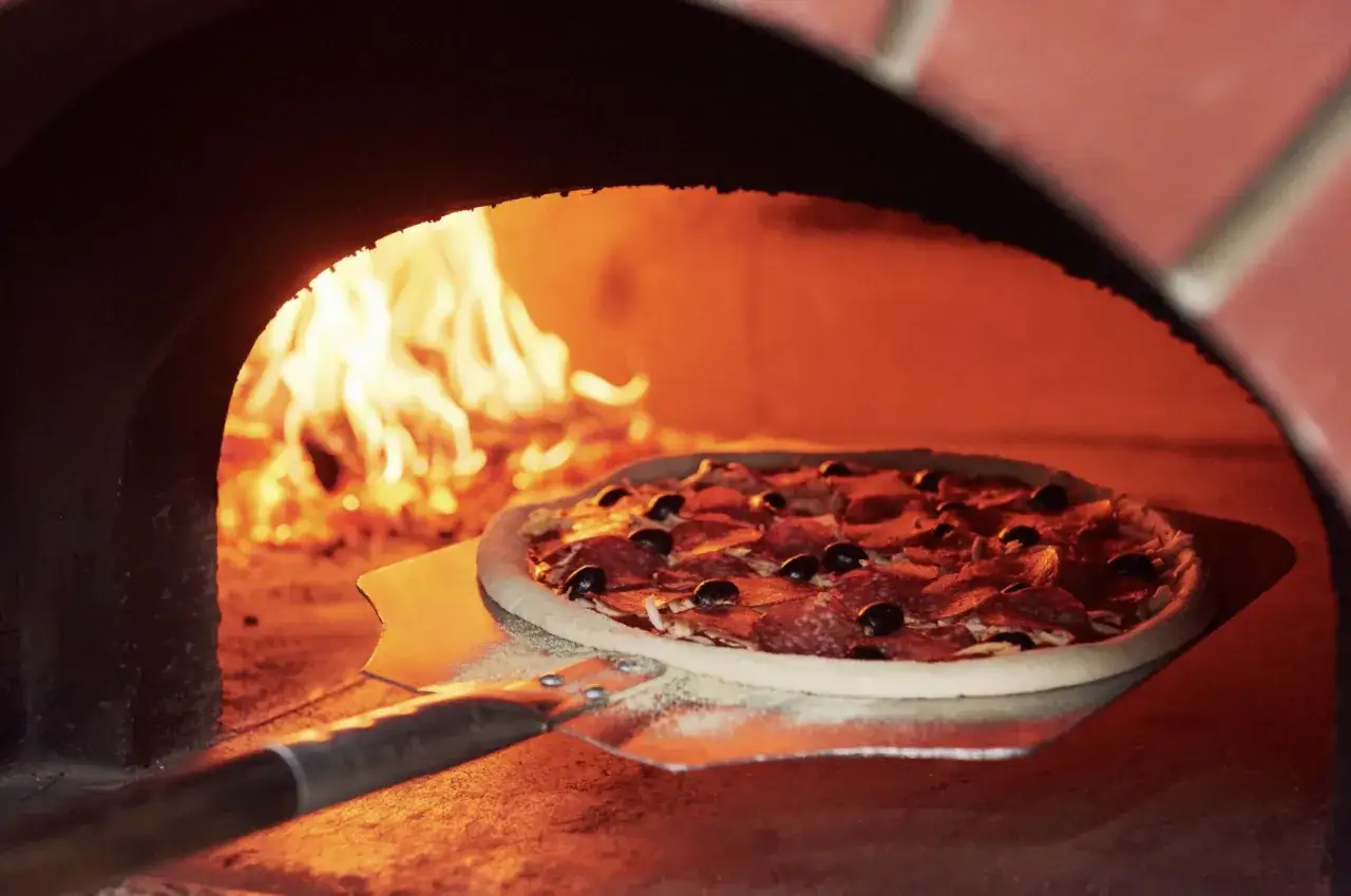 pizza wkładana do rozgrzanego pieca opalanego drewnem